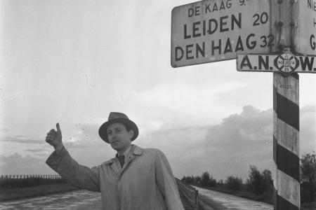 Man hitchhiking below a road sign